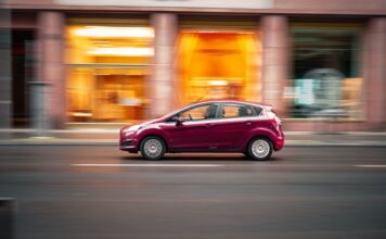Toyota Corolla czy Yaris? Który kompakt lepiej sprawdzi się w mieście Czerwony miejski samochód jedzie dynamicznie po ulicy w centrum miasta