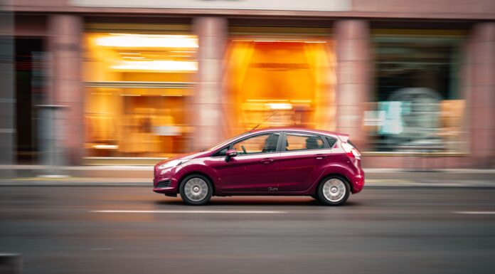 Toyota Corolla czy Yaris? Który kompakt lepiej sprawdzi się w mieście Czerwony miejski samochód jedzie dynamicznie po ulicy w centrum miasta