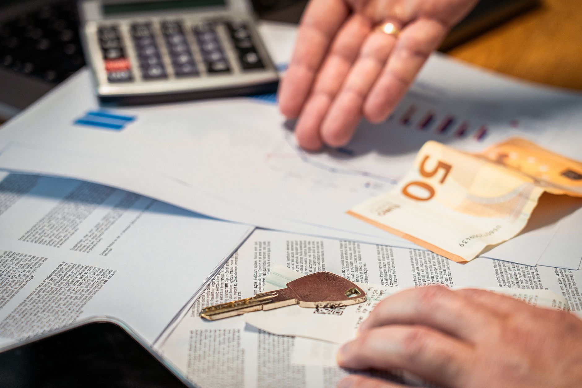Dłonie analizujące dokumenty finansowe, banknot 50 euro i kluczyk