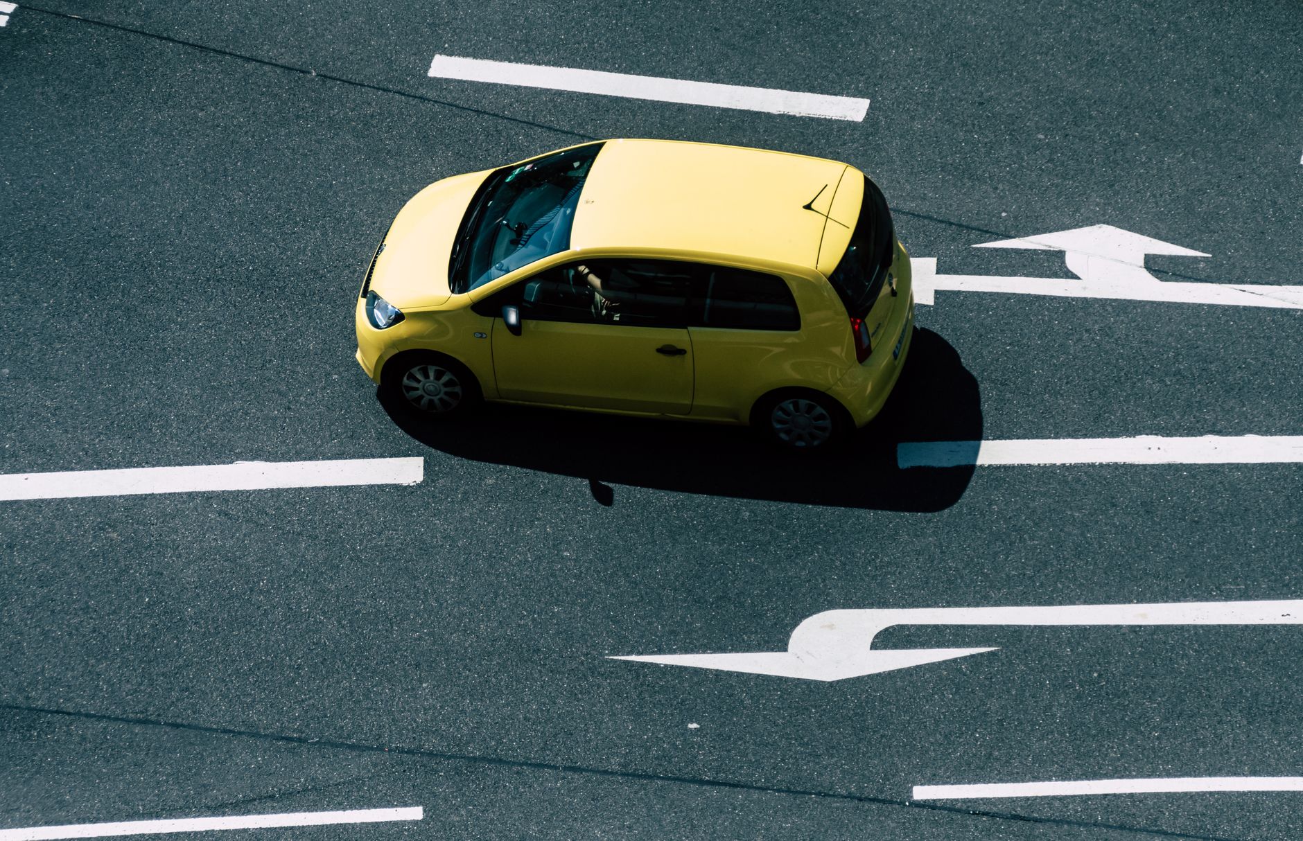 Żółte auto na miejskiej drodze z namalowanymi strzałkami kierunkowymi
